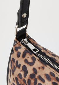 Sac à main en toile de léopard avec un matériau en cuir suédé texturé beige, arborant une fermeture éclair noire et des accents de bandoulière en cuir lisse.