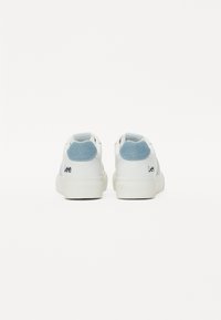 Zapatillas blancas con un acento de tela azul claro en el talón, con un diseño simple y detalles texturizados, etiquetadas con "Lee."