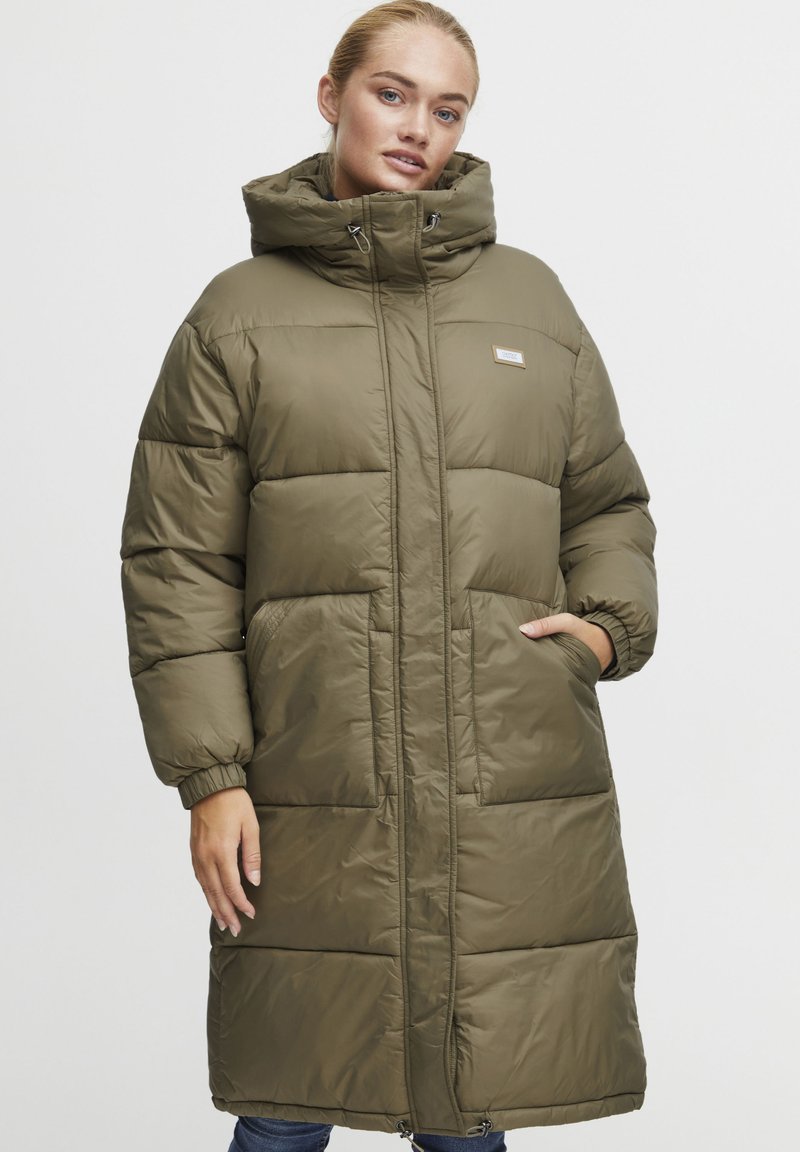 Manteau matelassé long, vert olive, en matériau brillant. Doté d'un col haut, d'une fermeture à l'avant et de deux poches latérales.