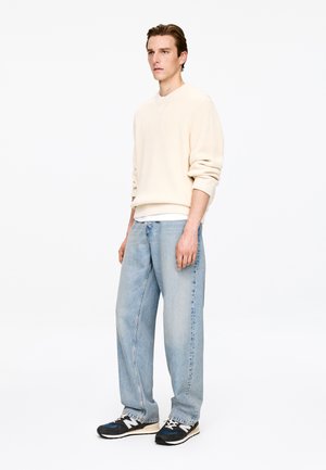 Kremowy prążkowany sweter, jasnoniebieskie luźne jeansy, czarno-białe trampki. Prosty design, casualowy krój, gładka faktura, bez charakterystycznych wzorów.