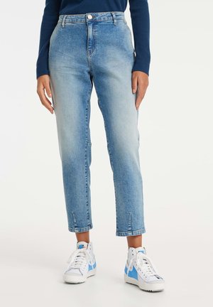 Jeans en denim bleu clair à taille haute, coupe droite, et deux poches avant. Présentent un léger délavage et un ourlet brut. Associés à des baskets blanches.
