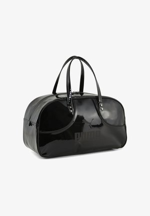 Bolso de viaje de charol negro con forma redondeada, asas dobles, cierre de cremallera y un sutil detalle de logo en la parte delantera. Textura suave y brillante.
