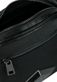 Borsa nera con zip in pelle texturizzata e tessuto. Presenta più zip e un accento metallico. L'interno mostra un rivestimento scuro.