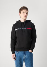 Svart hettegenser med kengurulomme og en fargerik horisontal stripe med røde og hvite detaljer. Laget av en bomullsblanding.