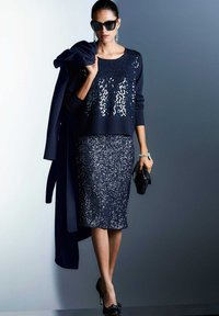 Navyblauwe sequinsweater met lange mouwen, gecombineerd met een bijpassende sequinpencilrok. Geaccessoireerd met een zwarte clutch en een zonnebril.