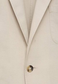 Blazer de lino beige con solapa muesca, cierre de un solo botón y un bolsillo parche. Textura suave con detalle de costura visible.