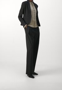 Ušitý černý blejzr přes béžový top se zvlněnými okraji, doplněný volnými černými kalhotami a špičatými černými lodičkami. Hladká textilie.