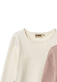 Chemise longue côtelée couleur crème avec col rond et étiquette "WHEAT", partiellement recouverte par une manche côtelée rose poussiére.