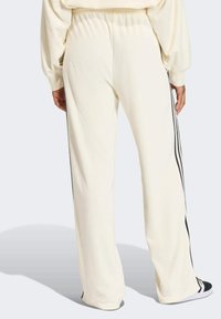 Krémové tepláky s volným střihem, s černými bočními pruhy a elastickým pasem pro pohodlí. Hladká textilie.