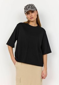 Sort løs T-shirt med korte ærmer, lavet af bomuld. Kombineret med en beige nederdel, tilbehør med en leopardmønstret kasket.