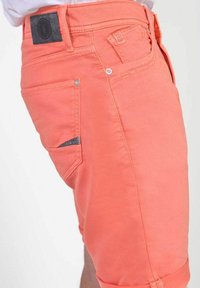 Koraalkleurige shorts met een gladde textuur, voorzien van een achterzak, zijzakken en opgerolde zomen. Metalen knoop en stiksels als accenten.