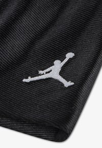 Juoda ribinė medžiaga su balta išsiuvinėta silueto atvaizdu, kuriame žmogus šoka ir laiko krepšinio kamuolį virš galvos.