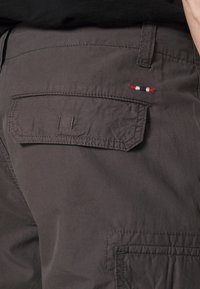 Shorts cargo gris avec une poche à l'arrière. Caractéristiques : couture soignée et un petit accent brodé en rouge, blanc et noir sur la poche.
