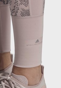 Detailní záběr na dolní část nohy v růžových legínách Adidas by Stella McCartney a k nim ladících pletených růžových teniskách se šňůrkami.