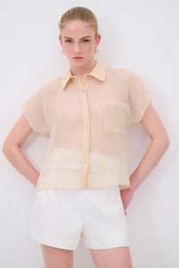 Camicia corta beige chiaro a maniche corte con tessuto trasparente e texturizzato, caratterizzata da chiusura a bottoni e una tasca sul petto.