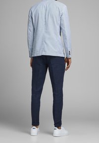 Modrá a bílá pruhovaná košile s dlouhými rukávy, doplněná tmavě námořnickými slim-fit kalhotami a bílými sportovními botami.