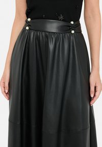 Gonna in ecopelle nera con vita arricciata. Presenta una cintura ampia con tre decorazioni in perla e una silhouette fluida.