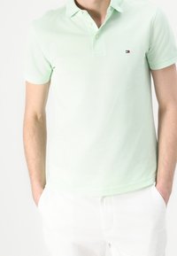 Jasnozielona koszulka polo wykonana z bawełny z teksturowanym wykończeniem, z kołnierzykiem na dwa guziki i małym logo po lewej stronie klatki piersiowej.