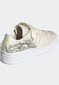 Cream-colored sneaker with a smooth satin finish, featuring white rubber sole, lace-up front, and graphic design on the side.