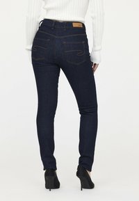 Dunkelblau Jeans aus Denim zeichnen sich durch ein schlankes Design aus, verfügen über zwei Gesäßtaschen mit geschwungener Naht und ein markiertes, braunes Lederpatch am Bund.