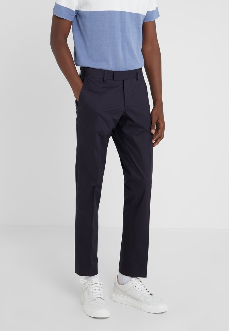 Marina byxor med skräddarsydd passform, slät tyg, bälteshännor och sidofickor. Bärs med en blå och vit blockfärgad skjorta och vita sneakers.