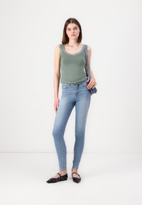 Green tank top with lace trim, light blue skinny jeans, and black pointed flats with circular cutouts. Simple design and fitted shape.
