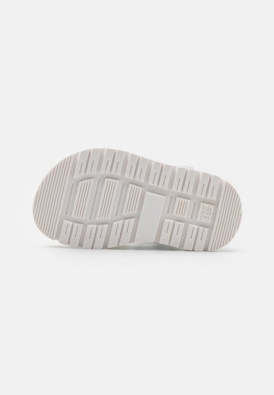 Shoe sole with a white rubber material, featuring a textured pattern for traction. Rounded edges and deep grooves enhance grip.