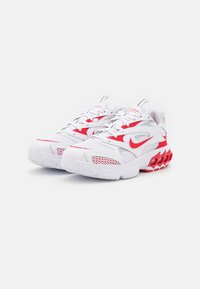 Valkoiset urheilusandaalit punaisilla yksityiskohdilla, verkkomateriaalia ylhäällä, pyöristetty kärki ja teksturoitu pohja. Sivussa erottuva Nike-logo.