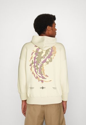 Lyse beige hoodie med et stort, farverigt abstrakt design i lilla, grøn og guld på ryggen. Har snoretræk i hætten og ribbede manschetter.