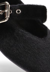 Zapato plano de pelo sintético negro con una correa de hebilla plateada y pequeños ojetes cerca de la abertura del tobillo.