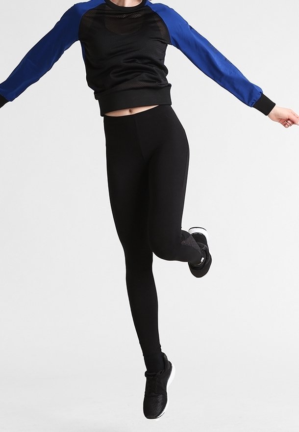 Personne portant un legging noir et un haut à manches longues noir et bleu, sautant avec une jambe pliée et les bras étendus.