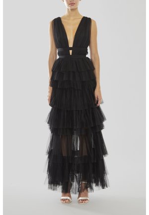 Robe en tulle noire avec un décolleté plongeant, des volants superposés et une taille cintrée, avec des sections transparentes et des sandales argentées à lanières.