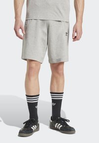 Gray cotton shorts with side pockets, featuring black branding. Black striped socks and black sneakers complete the outfit.