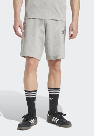 Šedé bavlněné šortky se bočními kapsami, ozdobené černým logem. Černé proužkované ponožky a černé tenisky dotvářejí celý outfit.