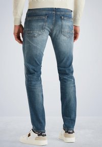 Vaqueros de mezclilla azul con un corte ajustado, que presentan un ligero desgaste, cinco bolsillos y costuras reforzadas, combinados con zapatillas blancas.