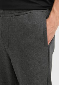 Grå joggebukser med en myk tekstur, elastisk midje og sidelommer. Materialet ser lett og pustende ut.