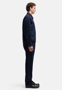 Granatowa kurtka dżinsowa i pasujące spodnie o luźnym kroju, z elastycznymi mankietami i bocznymi kieszeniami. Noszone z czarnymi butami sznurowanymi.