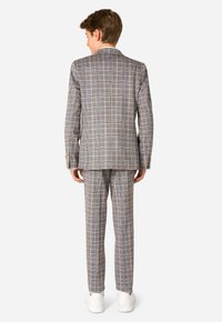 Completo a scacchi grigio con sottili righe viola e gialle, vestibilità sartoriale, spacco singolo sul retro, indossato con sneakers bianche.
