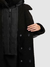 Fekete kabát, amely texturált polár külső réteggel, sima bélelt belső réteggel és fekete gombokkal rendelkezik, magas gallérral és cipzáras záródással.