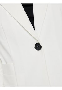 Bílý blazer s klopovým límcem, s jedním černým knoflíkem a postranní kapsou. Hladká textura, dobře padnoucí design a tvar.