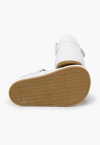 Weiße Lederkinderschuhe mit einem Klettverschluss, strukturiertem Gummisohle und dem eingravierten Markennamen auf der Unterseite. Größe 21.