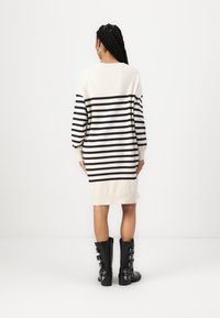 Beige and navy striped knitted dress with long sleeves, reaching mid-thigh. Worn with knee-high black leather buckle boots.