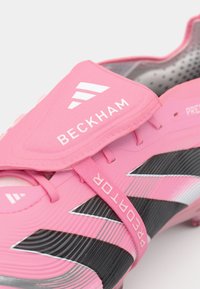 Roze Predator voetbalschoen met een gestructureerde bovenkant, zwarte accenten, witte branding en een gevoerde kraag voor comfort en ondersteuning.