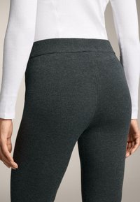 Szare legginsy z miękkiego, elastycznego materiału i szerokim, elastycznym pasem, pokazane z tyłu, w połączeniu z białą bluzką z długim rękawem.