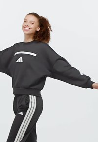 Black sweatshirt with a wide fit, featuring a white graphic across the chest and white stripe accents on black pants. Soft fabric texture.
