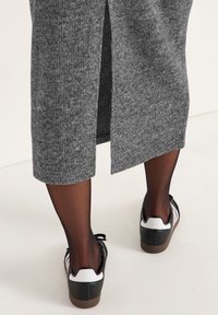 Grijze geribbelde gebreide jurk met een zijsplit, gecombineerd met zwart-witte sneakers met een gestructureerde zool en veters. Onder de jurk worden zwarte panty's gedragen.