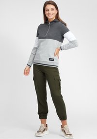 Felpa con cappuccio grigia e bianca, con zip a metà e logo, abbinata a pantaloni cargo color oliva e sneakers alla moda. Texture liscia, design casual.