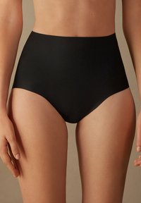 Des sous-vêtements noirs taille haute présentent une texture lisse, un design couvrant intégralement et des bords sans coutures pour un ajustement moderne.