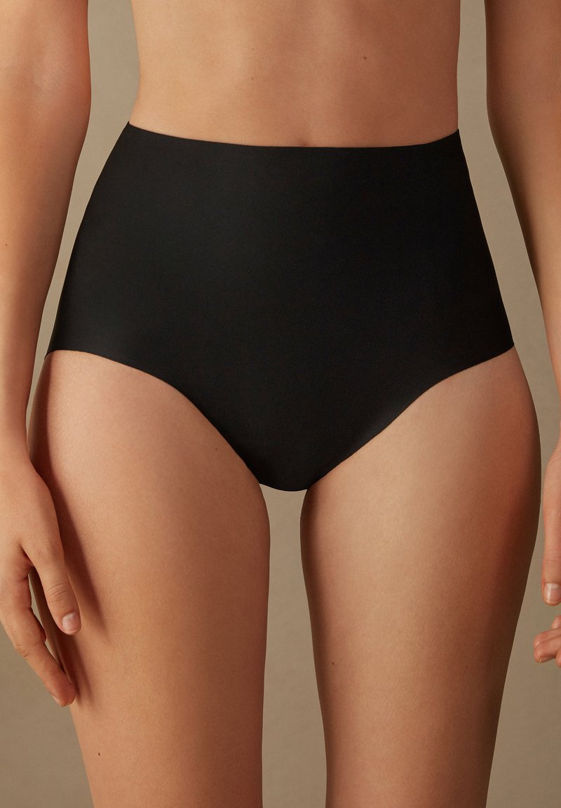 Des sous-vêtements noirs taille haute présentent une texture lisse, un design couvrant intégralement et des bords sans coutures pour un ajustement moderne.