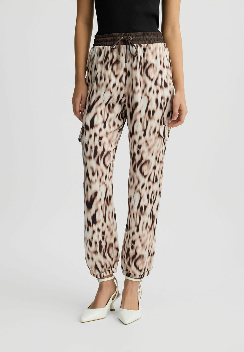 Lette, elastiske bukser med en beige og brun leopardmønster, der har manchetter ved anklerne og en snor med gyldne detaljer.